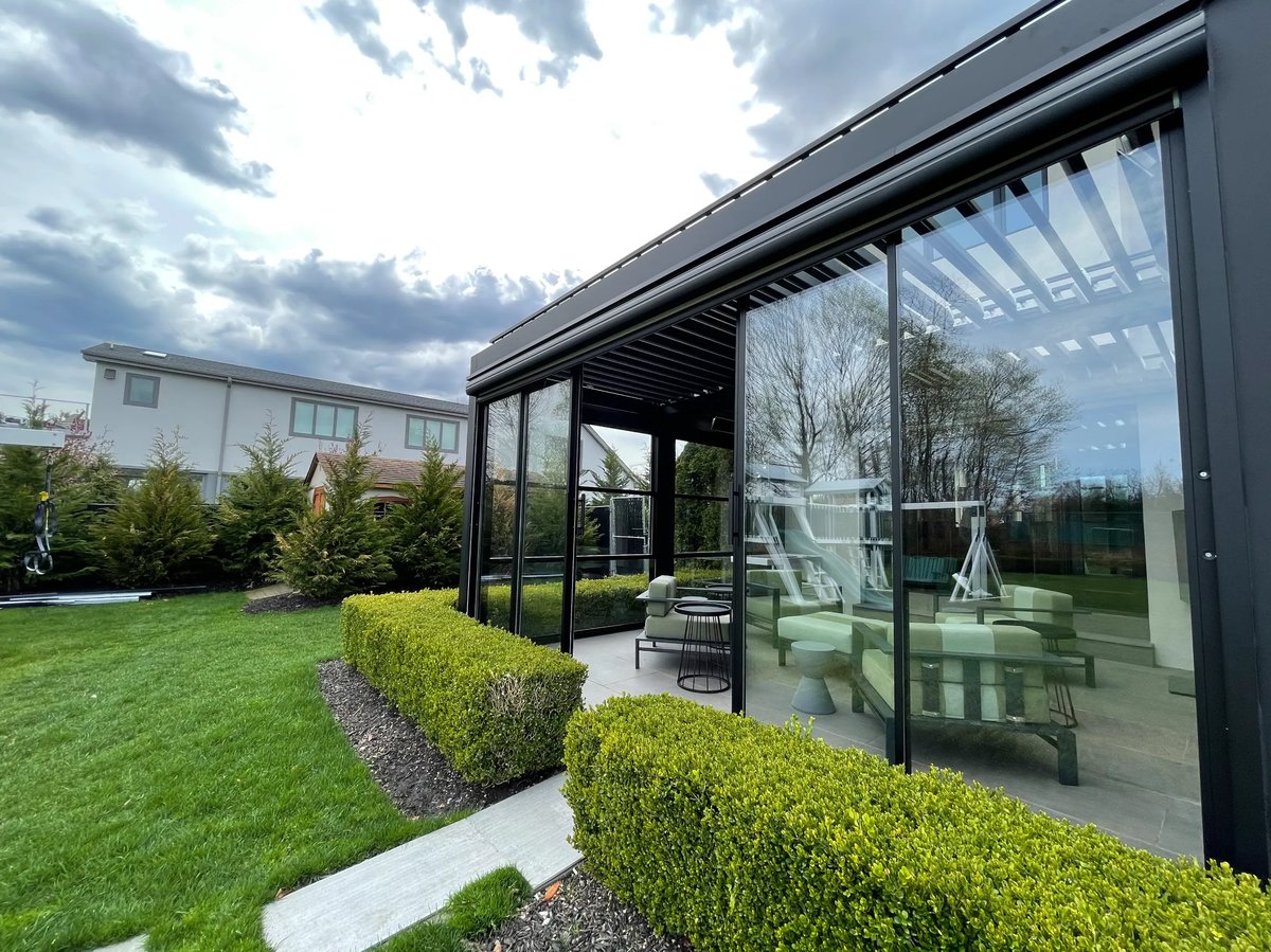 A contemporary residence featuring guillotine window walls, showcasing a glass-encased design and an inviting patio area