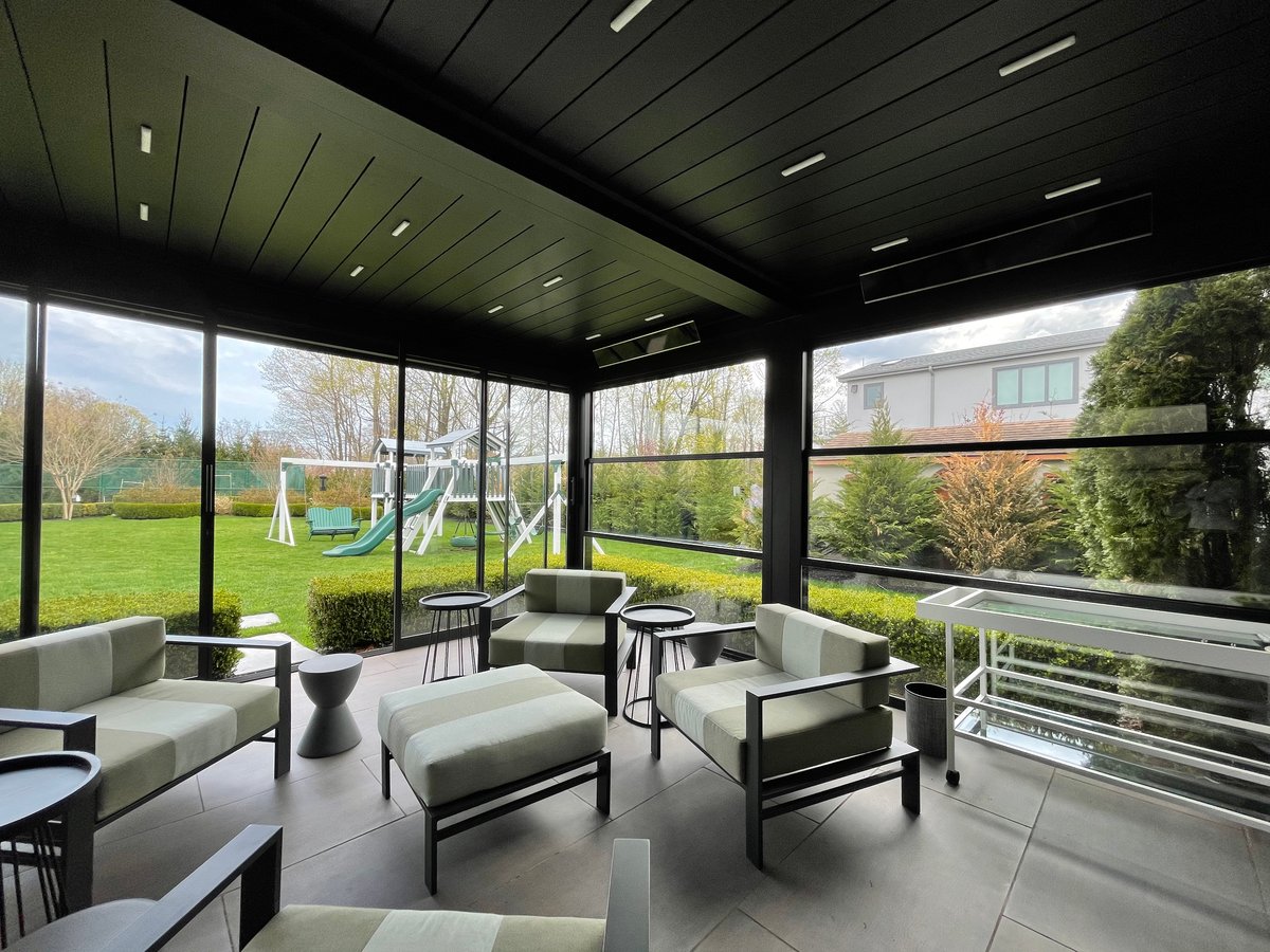 A screened porch with black furnishings and glass windows, featuring a guillotine glass door for easy access