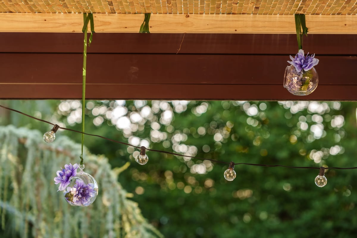 A decorative glass vase suspended from above, showcasing vibrant purple flowers, serving as an elegant adornment for a sukkah