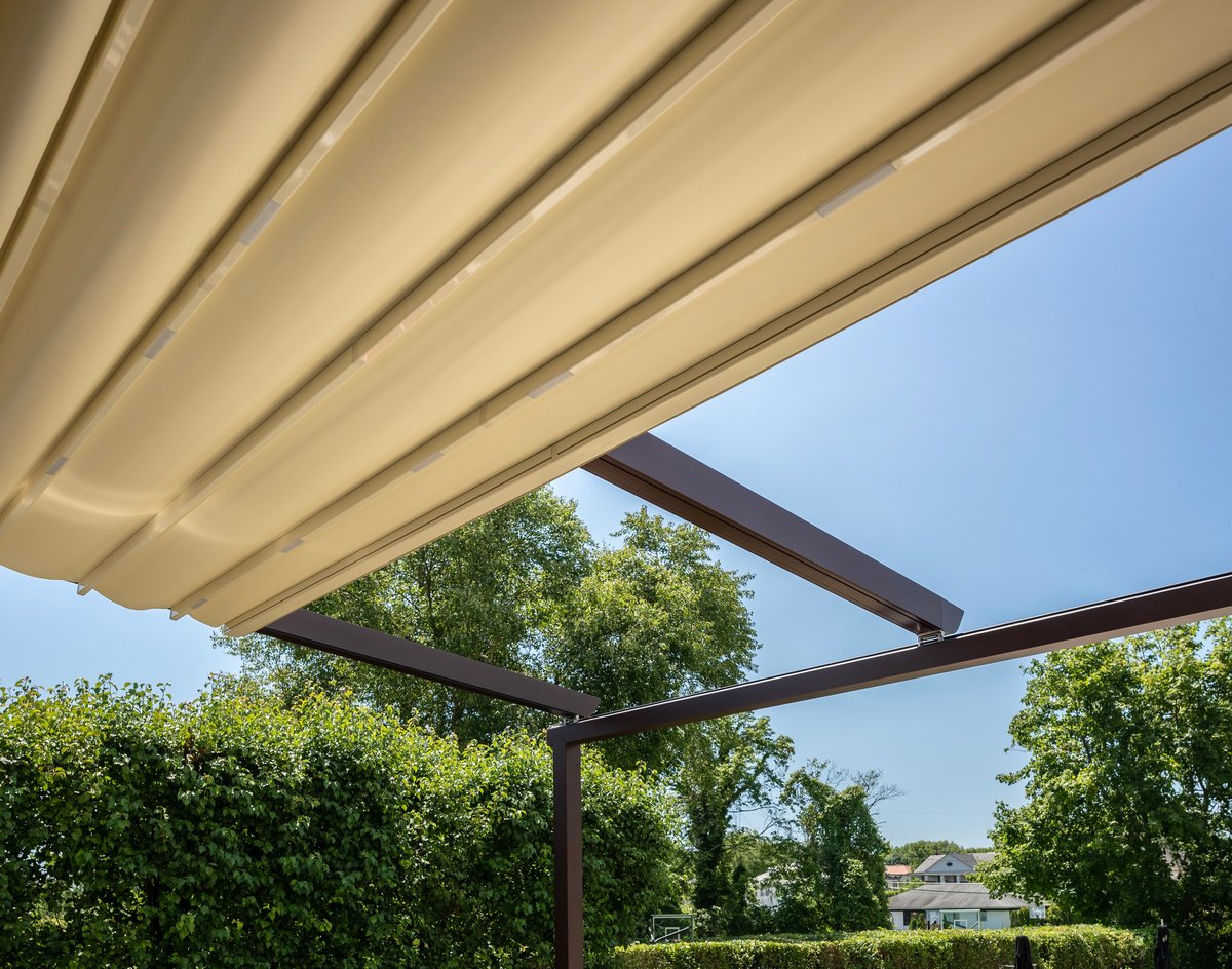 Pergola with retractable canopy in the backyard of the house with a table and sofas