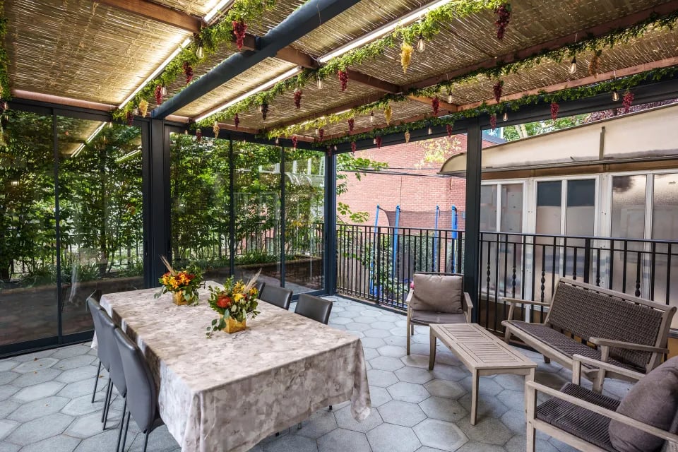 A covered pergola with a table and chairs on a patio, adorned with Sukkah decorations