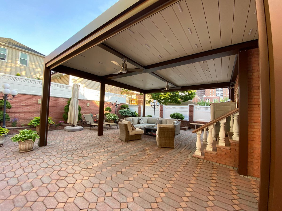 A seating area on a patio under a louvered pergola with ceiling fan