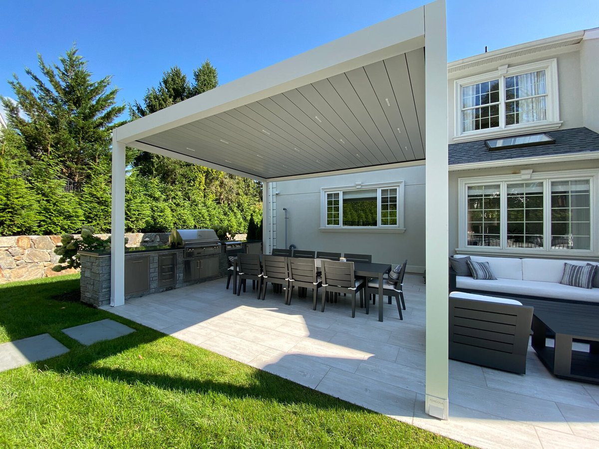 A large white house with a louvered pergola in the backyard